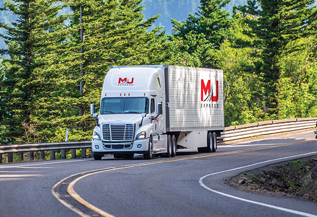 Transport truck driving on the road with scenic forest in the background.